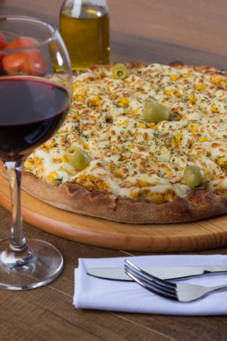 Akılda kalıcı tavuk aromalı pizza. Mozarella, tavuk, krem peynir, yeşil zeytin, mısır ve kırmızı domates sosuyla yapılmış. Kırmızı şarap ve zeytinyağıyla servis edilir. Çatal ve bıçak beyaz peçeteye. Dikey fotoğrafçılık.