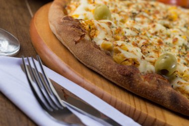 Akılda kalıcı tavuk aromalı pizza. Mozarella, tavuk, krem peynir, yeşil zeytin, mısır ve kırmızı domates sosuyla yapılmış. Çatal ve bıçak beyaz peçeteye. Dinamik açılı yatay fotoğrafçılık.