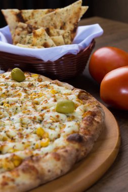 Ahşap bir tahtanın üzerinde servis edilen Catupiry Chicken aromalı pizza. Mozarella, tavuk, krem peynir, yeşil zeytin, mısır ve kırmızı domates sosuyla yapılmış. Arka planda aperatifler ve domatesler. Dikey fotoğrafçılık.