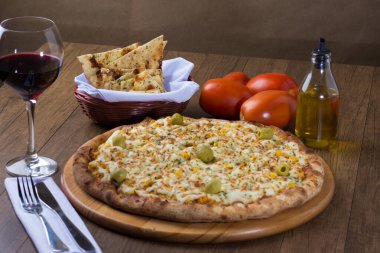 Ahşap bir tahtanın üzerinde servis edilen Catupiry Chicken aromalı pizza. Mozarella, tavuk, krem peynir, yeşil zeytin, mısır ve kırmızı domates sosuyla yapılmış. Bir bardak kırmızı şarap, crostini, zeytinyağı. fotoğrafçılık