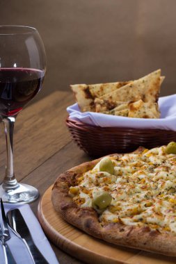 Ahşap bir tahtanın üzerinde servis edilen Catupiry Chicken aromalı pizza. Mozarella, tavuk, krem peynir, yeşil zeytin, mısır ve kırmızı domates sosu. Bir bardak kırmızı şarap ve crostini. Dikey fotoğrafçılık 2.