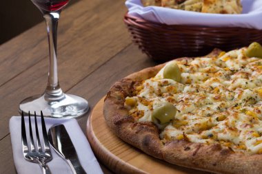Ahşap bir tahtanın üzerinde servis edilen Catupiry Chicken aromalı pizza. Mozarella, tavuk, krem peynir, yeşil zeytin, mısır ve kırmızı domates sosu. Bir bardak kırmızı şarap ve crostini. Yatay Fotoğrafçılık.