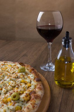 Tahta bir tahtanın üzerinde servis edilen lezzetli tavuk aromalı pizza. Mozarella, tavuk, krem peynir, yeşil zeytin, mısır ve kırmızı domates sosuyla yapılmış. Bir kadeh kırmızı şarap, zeytinyağı..