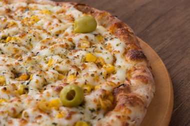 Tahta bir tahtanın üzerinde servis edilen lezzetli tavuk aromalı pizza. Mozarella, tavuk, krem peynir, yeşil zeytin, mısır ve kırmızı domates sosuyla yapılmış. Tipik İtalyan yemekleri..