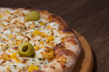 Tahta bir tahtanın üzerinde servis edilen lezzetli tavuk aromalı pizza. Mozarella, tavuk, krem peynir, yeşil zeytin, mısır ve kırmızı domates sosuyla yapılır..