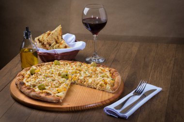 Tahta bir tahtanın üzerinde servis edilen lezzetli tavuk aromalı pizza. Mozarella, tavuk, krem peynir, yeşil zeytin, mısır ve kırmızı domates sosuyla yapılmış. Bir bardak şarap, bir porsiyon crostini.,