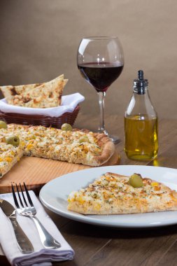 Tahta bir tahtanın üzerinde servis edilen lezzetli tavuk aromalı pizza. Mozarella, tavuk, krem peynir, yeşil zeytin, mısır ve kırmızı domates sosuyla yapılmış. Bir kadeh şarap.,