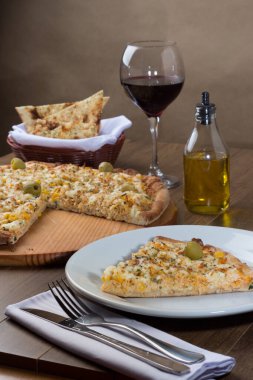 Tahta bir tahtanın üzerinde servis edilen lezzetli tavuk aromalı pizza. Mozarella, tavuk, krem peynir, yeşil zeytin, mısır ve kırmızı domates sosuyla yapılmış. Bir bardak şarap, bir porsiyon crostini..
