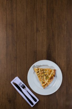 Tahta bir tahtanın üzerinde servis edilen lezzetli tavuk aromalı pizza. Mozarella, tavuk, krem peynir, yeşil zeytin, mısır ve kırmızı domates sosuyla yapılmış. Beyaz tabakta bir dilim pizza..