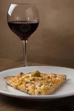 Tahta bir tahtanın üzerinde servis edilen lezzetli tavuk aromalı pizza. Mozarella, tavuk, krem peynir, yeşil zeytin, mısır ve kırmızı domates sosuyla yapılmış. Beyaz tabakta servis edilen bir dilim pizza.