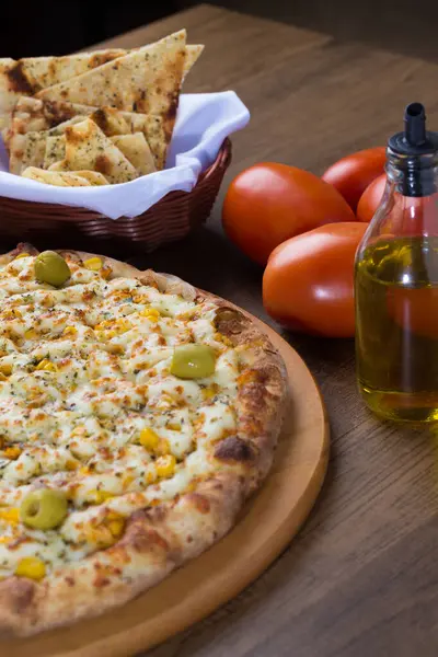 Ahşap bir tahtanın üzerinde servis edilen Catupiry Chicken aromalı pizza. Mozarella, tavuk, krem peynir, yeşil zeytin, mısır ve kırmızı domates sosuyla yapılmış. Yanında zeytinyağı ile birlikte aperatif crostini porsiyonu. Yatay Fotoğrafçılık.