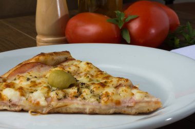 Gratin Loin Pizza. Mozzarella, Kanada usulü sığır filetosu, kremalı süt ve yeşil zeytin. Beyaz tabakta servis edilmiş. Karabiber, fesleğen, zeytinyağı, çatal ve bıçak öğütücü. İtalyan tipik yemekleri.