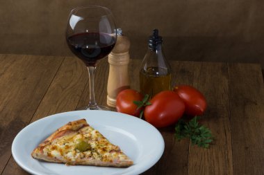 Lezzetli Gratin biftekli pizza. Mozzarella, Kanada usulü sığır filetosu, kremalı süt ve yeşil zeytin. Beyaz tabakta servis edilmiş. Şarap, Kara Biber Öğütücü, Fesleğen, Zeytinyağı, Çatal ve Bıçak.