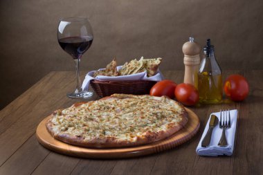 Gratin Loin Pizza. Mozzarella, Kanada usulü sığır filetosu, kremalı süt ve yeşil zeytin. Yanında bir bardak kırmızı şarap, bir porsiyon crostini, kırmızı domates, zeytinyağı, karabiber öğütücü, çatal ve bıçak..