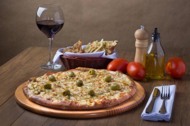 Gratin Loin Pizza. Mozzarella, Kanada usulü sığır filetosu, kremalı süt ve yeşil zeytin. Yanında bir bardak kırmızı şarap, bir porsiyon crostini, kırmızı domates, zeytinyağı, karabiber öğütücü ve çatal bıçak takımı.