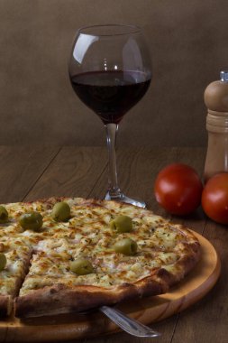 Tahta tahtada servis edilen Gratin Sirloin Pizza. Mozzarella, Kanada usulü sığır filetosu, kremalı süt ve yeşil zeytin. Pizza servis ediliyor. Şarap kadehi, karabiber öğütücü, fesleğen, maydanoz, çatal ve bıçak..