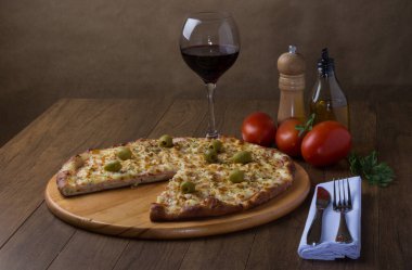Tahta tahtada servis edilen Gratin Sirloin Pizza. Mozzarella, Kanada usulü sığır filetosu, kremalı süt ve yeşil zeytin. Pizza servis ediliyor. Bir bardak şarap, karabiber öğütücü, fesleğen, maydanoz, zeytinyağı.