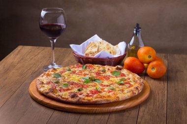 Lezzetli pizza hamuru, Mozzarella, domates, marjoram ve yeşil zeytinle yapılmış pizza. Tahta bir tahtanın üzerinde servis edilmiş. Napoli Pizzası. Kırmızı şarap, crostini, zeytinyağı.