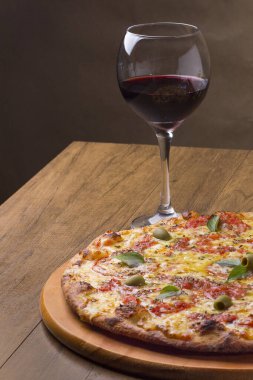 Lezzetli pizza hamuru, Mozzarella, domates, marjoram ve yeşil zeytinle yapılmış pizza. Tahta bir tahtanın üzerinde servis edilmiş. Napoli Pizzası. Kristal bardakta servis edilen kırmızı şarap..