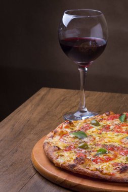 Lezzetli pizza hamuru, Mozzarella, domates, marjoram ve yeşil zeytinle yapılmış pizza. Tahta bir tahtanın üzerinde servis edilmiş. Napoli Pizzası. Cam bir kasede servis edilen kırmızı şarap. Dikey fotoğraf.