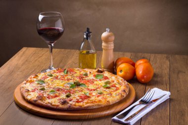 Lezzetli pizza hamuru, Mozzarella, domates, marjoram ve yeşil zeytinle yapılmış pizza. Tahta bir tahtanın üzerinde servis edilmiş. Napoli Pizzası. Kırmızı şarap, crostini, zeytinyağı, çatal ve bıçak. Dikey fotoğraf.