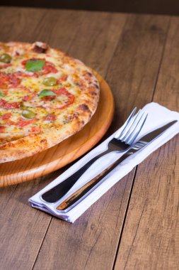 Lezzetli pizza hamuru, Mozzarella, domates, marjoram ve yeşil zeytinle yapılmış pizza. Tahta bir tahtanın üzerinde servis edilmiş. Napoli Pizzası. Çatal ve bıçak peçeteye. Dikey Fotoğraf.