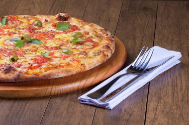 Lezzetli pizza hamuru, Mozzarella, domates, marjoram ve yeşil zeytinle yapılmış pizza. Tahta bir tahtanın üzerinde servis edilmiş. Napoli Pizzası. Çatal ve bıçak peçeteye..