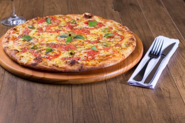 Lezzetli pizza hamuru, Mozzarella, domates, marjoram ve yeşil zeytinle yapılmış pizza. Tahta bir tahtanın üzerinde servis edilmiş. Napoli Pizzası. Çatal ve bıçak peçeteye. Fotoğraf pizzası..