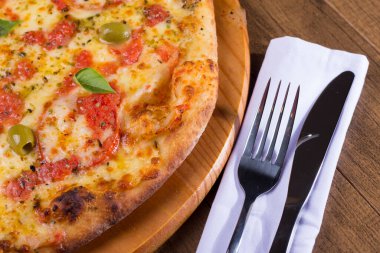 Lezzetli pizza hamuru, Mozzarella, domates, marjoram ve yeşil zeytinle yapılmış pizza. Tahta bir tahtanın üzerinde servis edilmiş. Napoli Pizzası. Çatal ve bıçak peçeteye. Makro Fotoğraf.