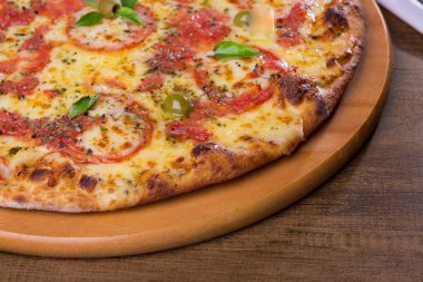 Lezzetli pizza hamuru, Mozzarella, domates, marjoram ve yeşil zeytinle yapılmış pizza. Tahta bir tahtanın üzerinde servis edilmiş. Napoli Pizzası. Sol üst hizalı pizza. Yatay.