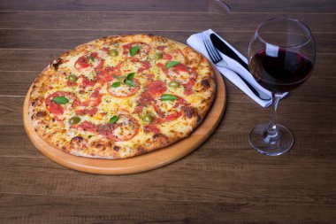 Lezzetli pizza hamuru, Mozzarella, domates, marjoram ve yeşil zeytinle yapılmış pizza. Tahta bir tahtanın üzerinde servis edilmiş. Napoli Pizzası. Çatal ve bıçak. Bir kadeh kırmızı şarap. Rafine edilmiş gastronomi.