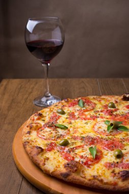 Lezzetli pizza hamuru, Mozzarella, domates, marjoram ve yeşil zeytinle yapılmış pizza. Tahta bir tahtanın üzerinde servis edilmiş. Napoli Pizzası. Bir kadeh kırmızı şarap. Yenilenmiş gastronomi. Dikey Makro Fotoğraf