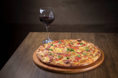 Lezzetli pizza hamuru, Mozzarella, domates, marjoram ve yeşil zeytinle yapılmış pizza. Tahta bir tahtanın üzerinde servis edilmiş. Napoli Pizzası. Bir kadeh kırmızı şarap. Yenilenmiş gastronomi. Yatay Fotoğraf