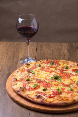 Lezzetli pizza hamuru, Mozzarella, domates, marjoram ve yeşil zeytinle yapılmış pizza. Tahta bir tahtanın üzerinde servis edilmiş. Napoli Pizzası. Gastronomi. Bir kadeh kırmızı şarap, üst dikey gurme fotoğrafı.