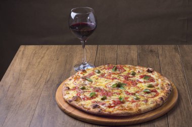 Lezzetli pizza hamuru, Mozzarella, domates, marjoram ve yeşil zeytinle yapılmış pizza. Tahta bir tahtanın üzerinde servis edilmiş. Napoli Pizzası. Gastronomi. Bir bardak kırmızı şarap, yatay fotoğrafın gurme fotoğrafı.