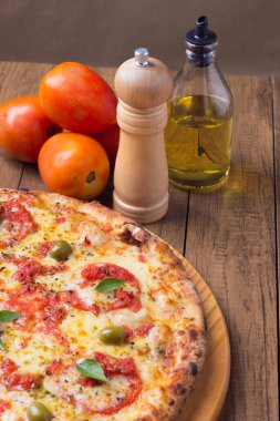 Lezzetli pizza hamuru, Mozzarella, domates, marjoram ve yeşil zeytinle yapılmış pizza. Tahta bir tahtanın üzerinde servis edilmiş. Napoli Pizzası. Biber öğütücü, zeytinyağı ve domates. Ağız sulandıran yemekler..
