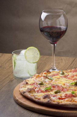 Lezzetli pizza hamuru, Mozzarella, domates, marjoram ve yeşil zeytinle yapılmış pizza. Tahtanın üzerinde. Napoli Pizzası. Bir kadeh kırmızı şarap. Limonlu soda ve buz küpleri. Gurme.