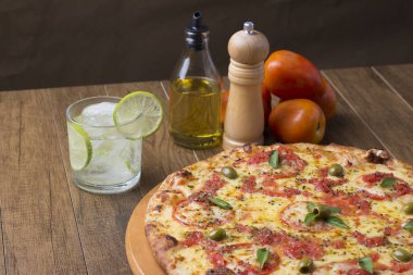 Lezzetli pizza hamuru, Mozzarella, domates, marjoram ve yeşil zeytinle yapılmış pizza. Tahtanın üzerinde. Napoli Pizzası. Limonlu soda ve buz küpleri. Gastronomik fotoğraf bırakıldı