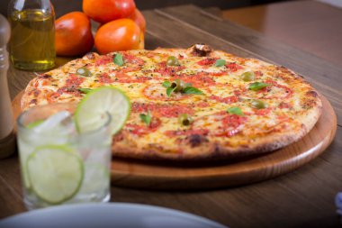 Lezzetli pizza hamuru, Mozzarella, domates, marjoram ve yeşil zeytinle yapılmış pizza. Tahtanın üzerinde. Napoli Pizzası. Buz çözeltisi ve limonlu karbonatlı su. domates