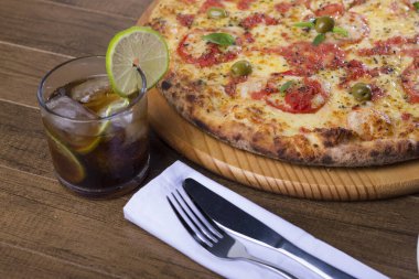 Mozzarella, domates, makarna ve yeşil zeytinle yapılmış bir pizza fotoğrafı. Napoli Pizzası. Süslemek için buzlu kola ve limon dilimi..