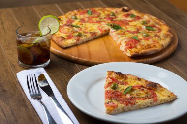 Mozzarella peyniri, domates, fesleğen yaprağı ve yeşil zeytinle yapılmış pizza dilimi. Napoli Pizzası. Tabakta servis edildi. Yanında limonlu kola ile. Çatal ve bıçak peçeteye