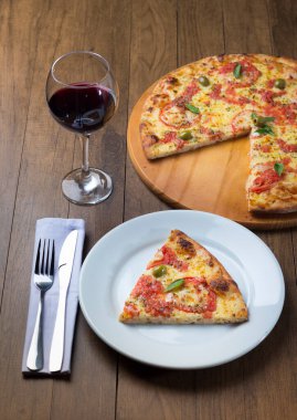 Mozzarella peynirli, domatesli, fesleğenli ve yeşil zeytinli pizza dilimi. Yanında da bir kadeh şarap var. Gurme gastronomi fotoğrafçılığı.