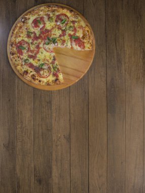 Mozzarella peynirli, domatesli, fesleğenli ve yeşil zeytinli pizza fotoğrafı ahşap bir tahtada servis ediliyor. Üst çekim.