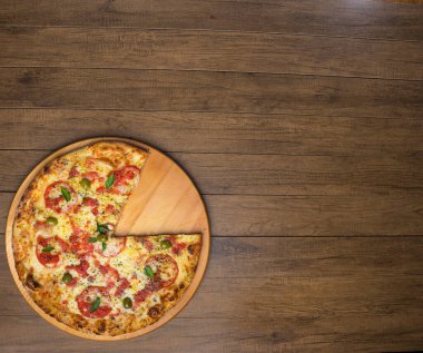 Mozzarella peynirli, domatesli, fesleğenli ve yeşil zeytinli pizza fotoğrafı ahşap bir tahtada servis ediliyor. Üstteki gurme fotoğrafı yatay konumda ve solda boşluk olan elementler var