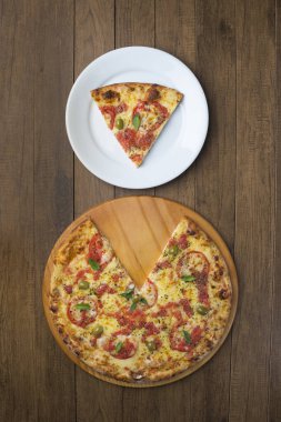 Mozzarella peyniri, domates, fesleğen yaprağı ve yeşil zeytinlerle yapılmış pizza Marguerita 'nın fotoğrafı ahşap bir tahtada servis ediliyor. Pizza dilimi üst köşedeki pizzayla aynı hizaya getirilmiş bir tabakta servis edilir..