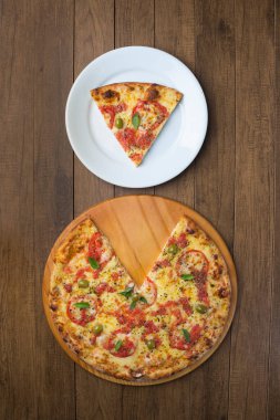 Saborosa Pizza Marguerita 'nın Mozzarella peyniri, domates, fesleğen yaprağı ve yeşil zeytinlerle yapılmış fotoğrafı ahşap bir tahtada servis ediliyor. Pizza dilimi tabağın üstünde servis edilir..