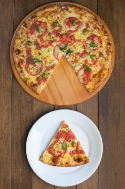 Mozzarella peyniri, domates, fesleğen yaprağı ve yeşil zeytinlerle yapılmış eğlenceli ve lezzetli bir pizza fotoğrafı ahşap bir tahtada servis ediliyor. Tabakta servis edilen pizza dilimi. İtalyan gastronomisi.