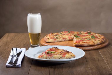 Mozzarella peynirli, domatesli, fesleğenli ve yeşil zeytinli pizza dilimi. Bir bardak bira, bulanık arka plan..