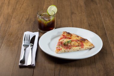 Mozzarella peyniri, domates, fesleğen yaprağı ve yeşil zeytinlerden yapılmış pizza dilimi. Bir bardak kola soda ve limon dilimleri. Ahşap fırında yapıldı..