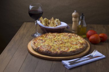 Bir bardak kırmızı şarap ve bir porsiyon crostini eşliğinde kırmızı domates dilimli lezzetli mozzarella peynirli pizza. Sağda kırmızı domatesler.